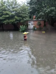 Ein Mann mit Regenschirm steht hüfthoch im Hochwasser 2021 in Köln Bickendorf in der Subbelrather Straße Höhe Lindweiler Hof.