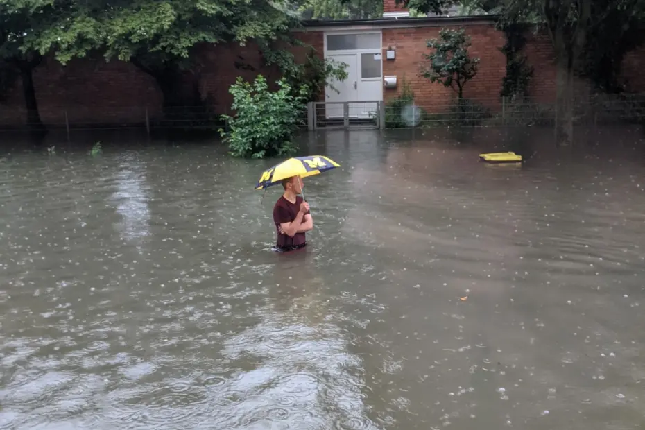 Ein Mann mit Regenschirm steht hüfthoch im Hochwasser 2021 in Köln Bickendorf in der Subbelrather Straße Höhe Lindweiler Hof.