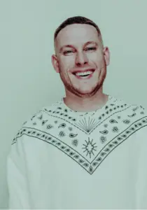 Portrait von Mo-Torres, Musiker aus Köln-Bickendorf, in einen weißen Winterpullover gekleidet und in die Kamera lachend. Copyright benhammer.